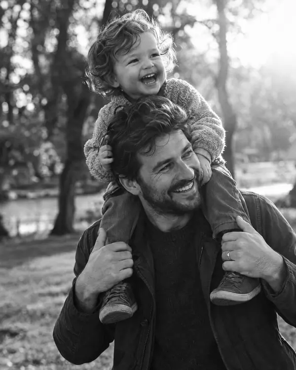 A dad carries his laughing toddler on his shoulders in a park.